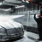 A woman expertly cleans a car using snow foam in a modern indoor car wash facility.
